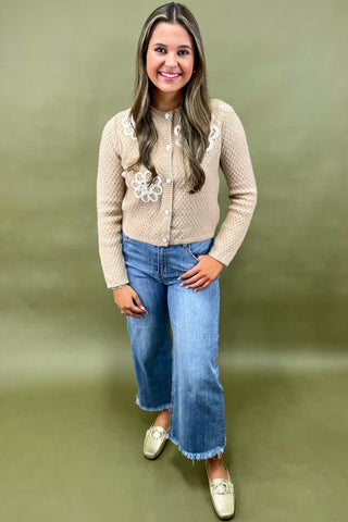 Woman wearing a beige knitted cardigan with floral patterns and blue jeans on a green background