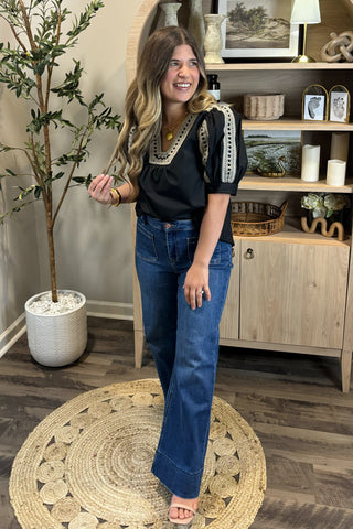 Woman in black top and blue jeans standing in a room with wooden flooring and decor.