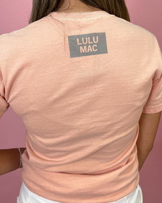 Person wearing a pink t-shirt with 'LULU MAC' logo on the back against a pink background