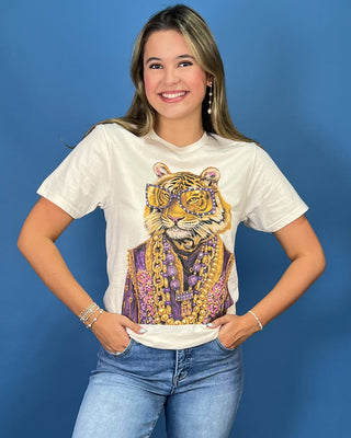 A woman wearing a white graphic t-shirt with a large gold and purple tiger print, paired with blue jeans, standing against a solid blue background.