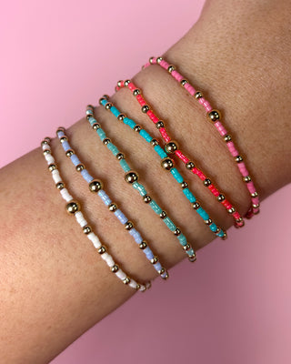 Multicolored beaded bracelets on a wrist with a pink background