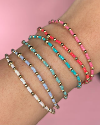 Set of colorful beaded bracelets on a wrist with a pink background