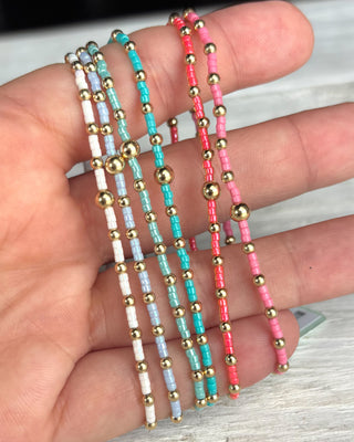 Three beaded bracelets in gold, turquoise, and pink on a hand.