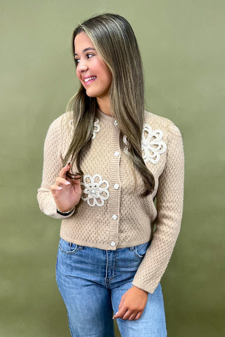 Woman wearing a beige cardigan with floral patterns against a green background