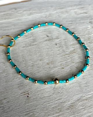 Turquoise beaded bracelet with gold accents on a light wooden surface