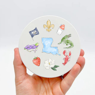 Round coaster with Louisiana-themed illustrations held by a hand on a light gray background