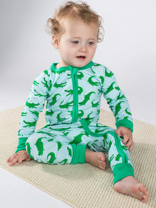 Baby wearing a green and blue dinosaur-patterned onesie on a white background