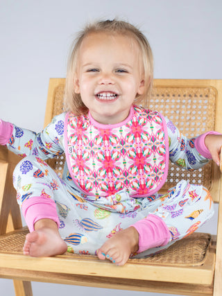 Child wearing a colorful bib and outfit sitting on a chair.