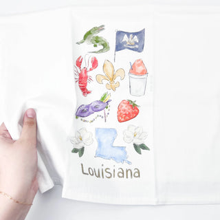 Hand holding a towel with Louisiana-themed designs on a white background