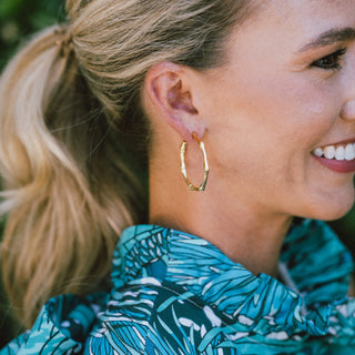 Woman wearing gold hoop earrings with a blurred natural background