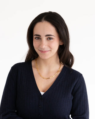 Woman wearing a dark blue sweater and gold necklace on a white background