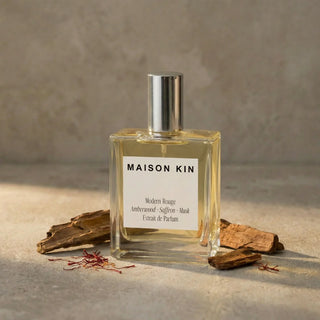 Maison Kin perfume bottle and packaging on a wooden surface with a blue background
