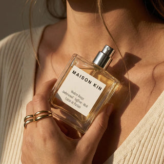 Person holding a Maison Kin perfume bottle with a neutral background
