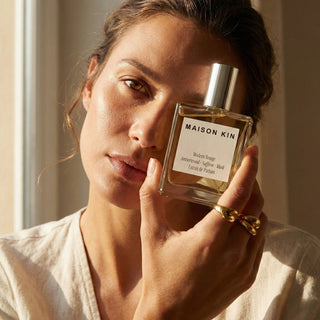 Woman holding a Maison Kin perfume bottle close to her face