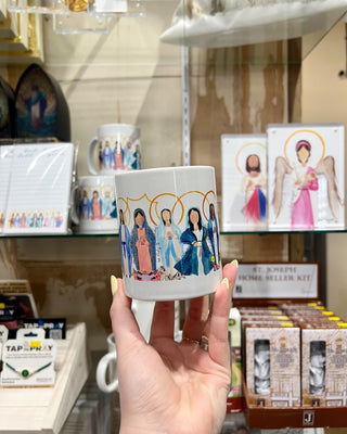 Hand holding a mug with illustrated figures in a store setting