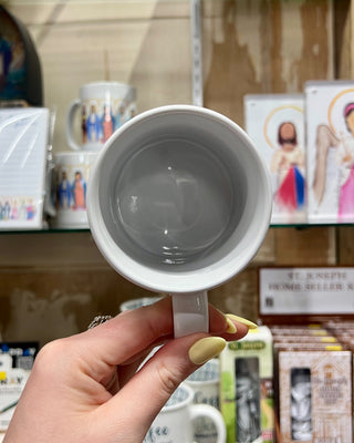White mug held by a hand with a blurred store background