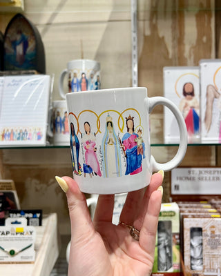 White mug with colorful illustrations held by a hand in a store setting