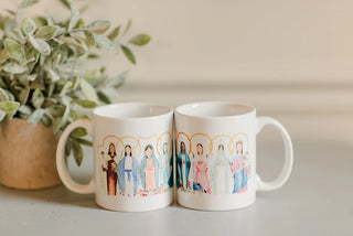 Two mugs with artistic illustrations of people on a light surface with a plant in the background