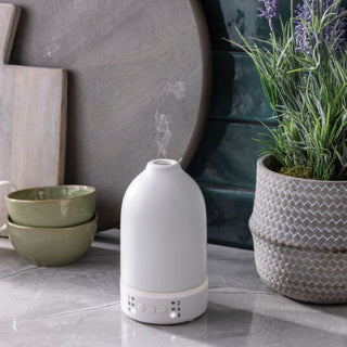 White diffuser on a stone surface with decorative items including bowls and a plant.