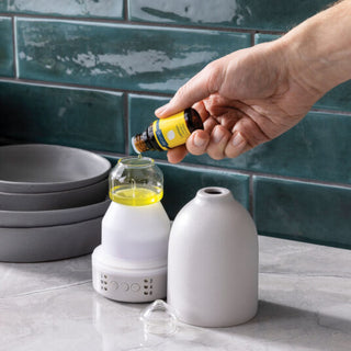 Person adding essential oil to a diffuser on a kitchen counter.