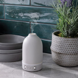 White diffuser emitting steam next to a potted plant on a tiled surface