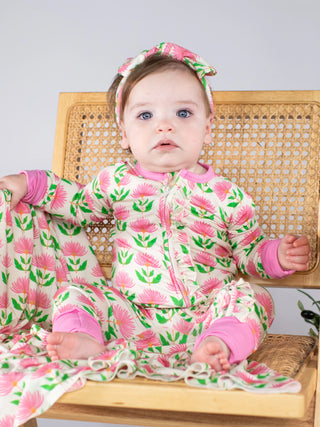 Baby wearing a pink and green floral onesie sitting on a wicker chair.