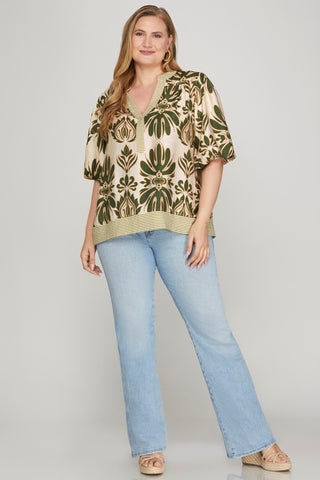 Woman wearing a patterned blouse and light blue jeans on a plain background