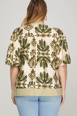 Woman wearing a patterned top with green and beige design on a plain background