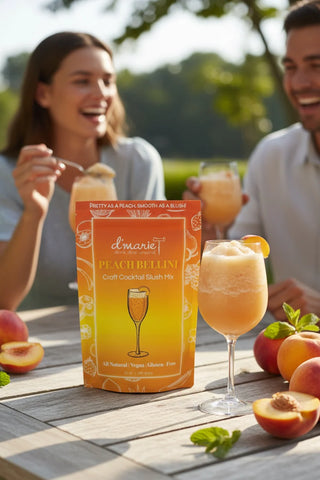 Two people enjoying peach bellini cocktails outdoors with a box of L'Marie Peach Bellini mix.