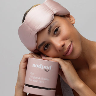 Woman wearing a pink sleep mask and holding a pink package with 'nodpod' branding.