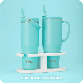 Two turquoise mugs with straws on a white stand against a light blue background, featuring the 'Swig' brand.