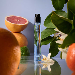 Perfume bottle with citrus fruits and flowers on a reflective surface