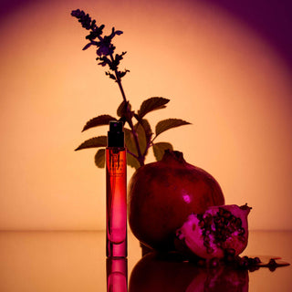 Perfume bottle with pomegranate and flowers on a reflective surface with a warm background