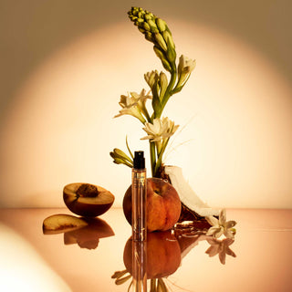 Perfume bottle with flowers and fruit on a reflective surface