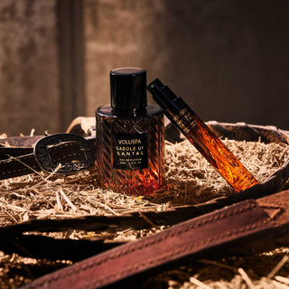 Two perfume bottles on a rustic background with a belt and hay.