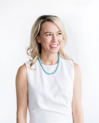 Woman wearing a white sleeveless top and turquoise beaded necklace on a white background