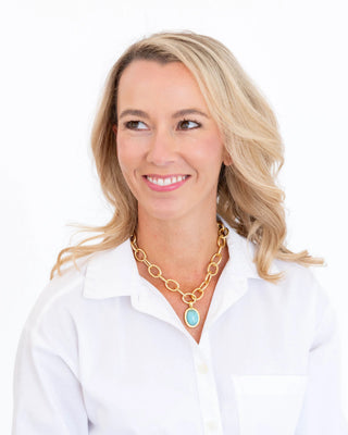 Woman wearing a gold necklace with a blue pendant on a white background