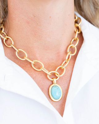 Gold chain necklace with a blue pendant worn by a person