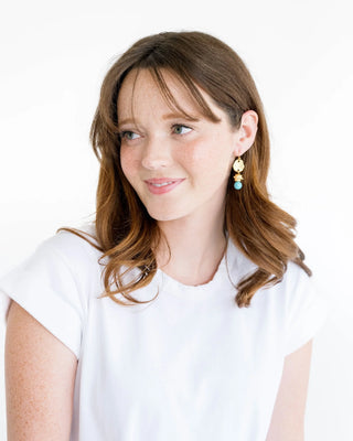 Gold and turquoise earrings on a Susan Shaw branded card against a pink background