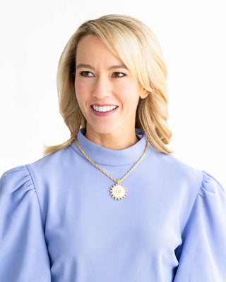 Woman wearing a light blue blouse with a necklace on a white background