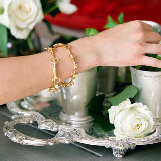 Gold bracelet on a wrist with a decorative silver tray and white roses in the background