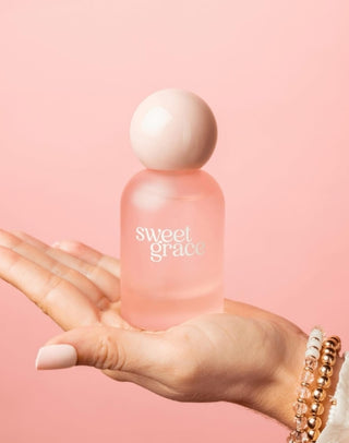 Hand holding a 'sweet grace' bottle against a pink background