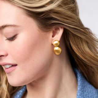 Close-up of a woman wearing gold double-ball earrings with a neutral background