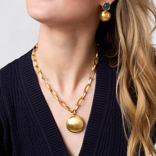 Gold necklace and earrings on a person wearing a dark blue cardigan.