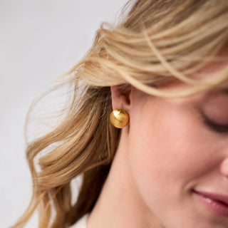 Close-up of a person wearing gold earrings with a neutral background