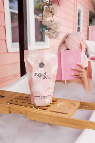 Bag of 'sweet grace' mineral soaping salts on a wooden tray with a pink house in the background.