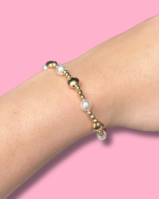 Gold and pearl bracelet on a wrist against a pink background
