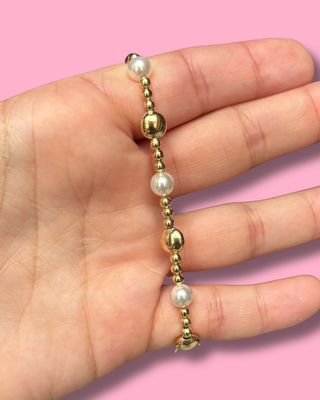 Gold and pearl beaded bracelet on a hand with a pink background