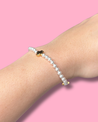 Pearl bracelet on a wrist against a pink background