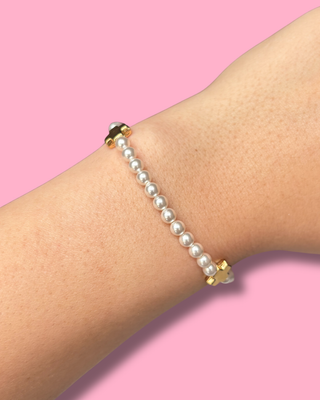 Pearl bracelet on a wrist with a pink background